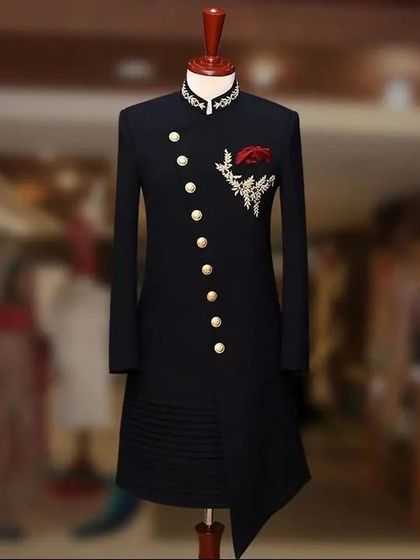 A sleek, black asymmetrical sherwani displayed on a mannequin. The design features a diagonal button placket and subtle embroidery, offering a modern and minimalist take on groom's wear.