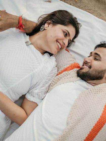 A sweet moment during a beach picnic, with the couple lying down and looking at each other with love. The yellow flower adds a pop of cheerful color.
