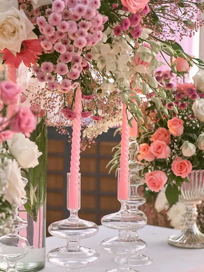 A detail shot of the elegant pink taper candles in modern glass holders, set against a backdrop of lush floral arrangements.