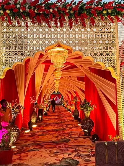 This royal entrance features a stunning arched gateway with intricate lattice work. The warm lighting inside the fabric tunnel creates a welcoming glow for arriving guests.
