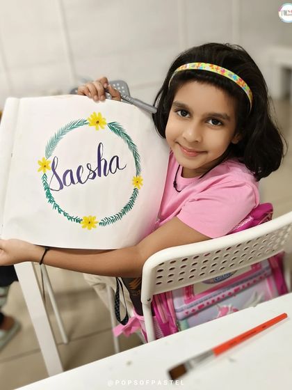 A young girl displays her personalized artwork, featuring her name beautifully lettered within a delicate floral wreath.
