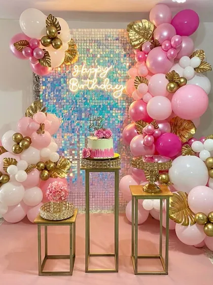 An elegant pink and gold themed party, perfect for an intimate home celebration. The decor features a shimmer wall, a neon sign, and a beautiful balloon arrangement with gold leaf details.