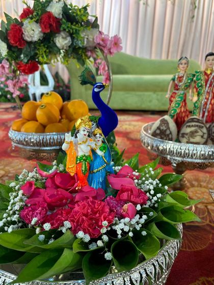 A centerpiece featuring a Radha-Krishna idol, surrounded by fresh flowers and peacock figures.