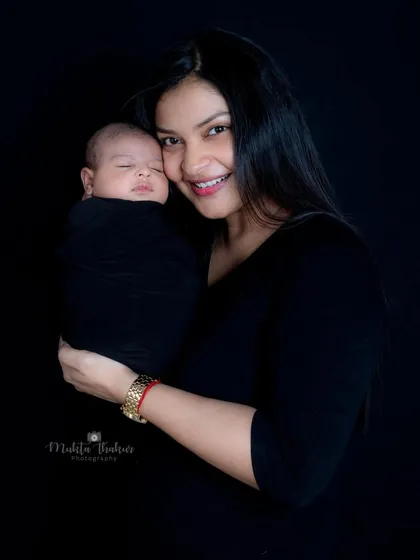 The beautiful smile of a new mother as she cuddles her sleeping baby, a perfect memory captured against a classic black studio backdrop.