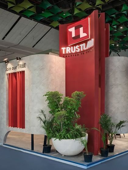 The exterior of the Trustlam stall features a bold combination of concrete-textured curvilinear walls and a striking red central element. This juxtaposition of materials and forms creates a memorable and modern facade.