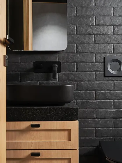 This guest bathroom features a custom light wood vanity with a black granite top. The textured black brick tiles and matte black fixtures create a bold, contemporary look that is both dramatic and refined.