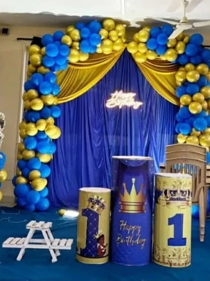 The prince-themed first birthday setup from another angle, showing the "Happy Birthday" neon sign and custom-printed plinths. The royal blue and gold color scheme creates a regal atmosphere.