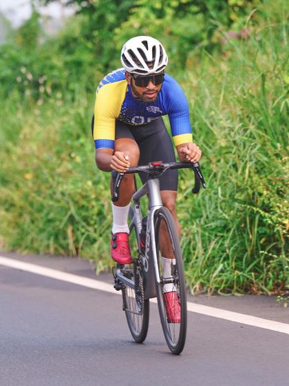 This shot freezes a cyclist in a full aerodynamic tuck, showcasing speed and form. The clean background and sharp focus on the rider highlight the individual effort within the team sport.