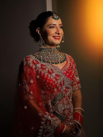 A smiling bride in her red lehenga, bathed in a warm, golden light. A classic portrait that radiates happiness.