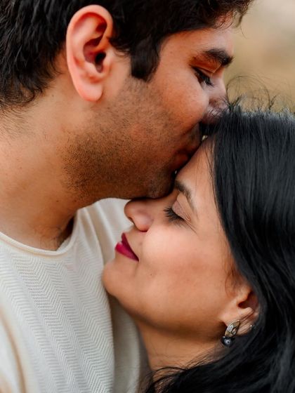 A close-up, intimate moment from a pre-wedding shoot. The focus is entirely on their connection, with a gentle forehead kiss conveying deep affection.