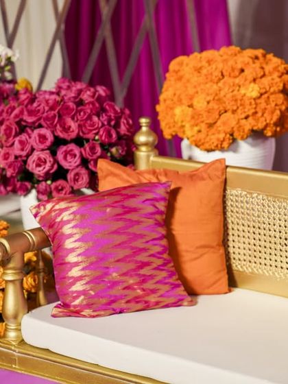 A detail of the seating, showing the golden bench, rattan back, and the vibrant brocade and silk cushions in shades of pink and orange.