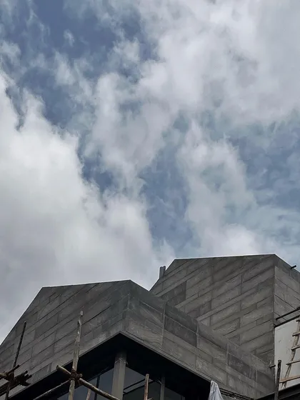 The angular form of a stone-clad roof against the sky. This work-in-progress shot shows the strong, sculptural quality of the building's facade taking shape.
