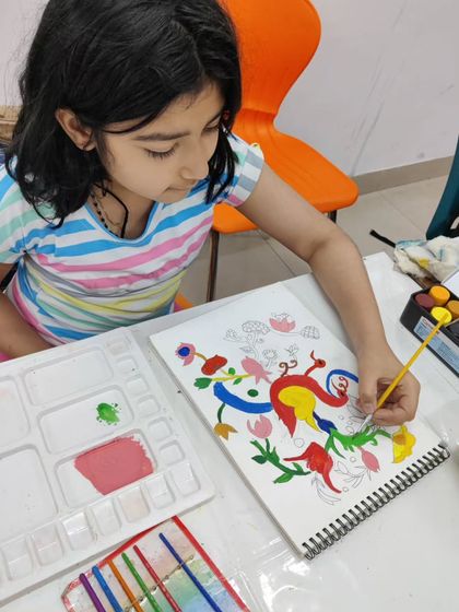 A young student learns a traditional Indian folk art style, carefully painting vibrant, stylized birds and flowers.