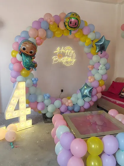 A pastel-themed 14th birthday with a Cocomelon touch. This home setup features a beautiful ring of pastel balloons, a neon sign, and large marquee numbers, showing how we can adapt themes for older kids too.