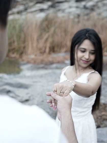 A 'follow me' style shot focusing on the couple's hands, with the bride leading the groom towards a natural, rocky landscape.