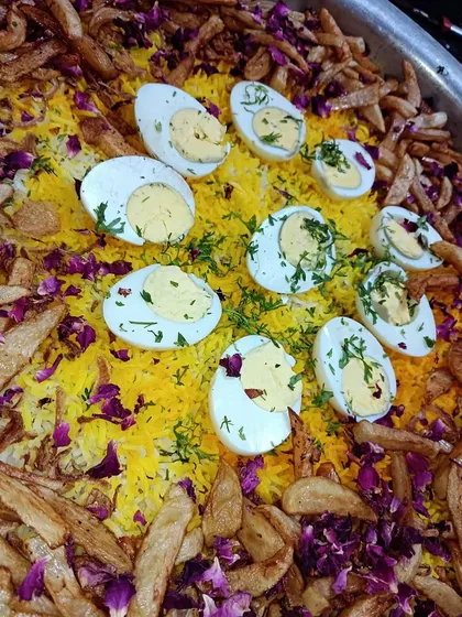 A colorful and festive biryani preparation, generously garnished with boiled eggs, crispy fries, and dried rose petals. Perfect for a celebration.