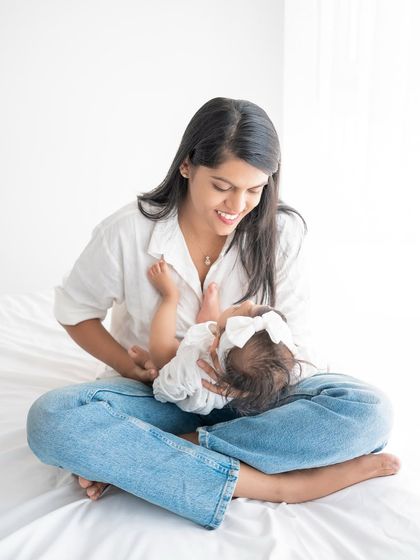 A mother playing with her baby on a bright white bed.