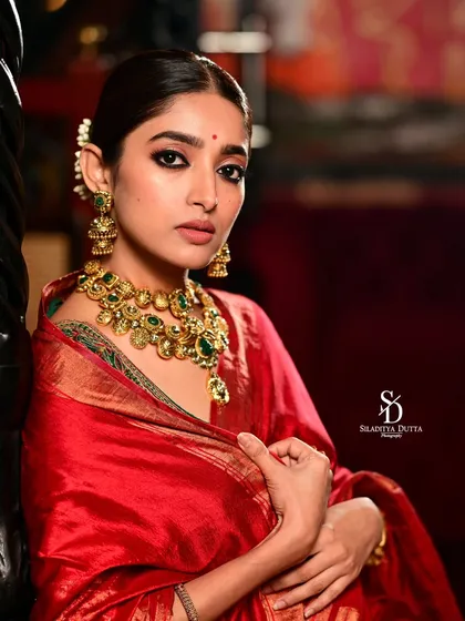 Actress Ishaa Saha looking regal in a red saree and elaborate green and gold jewellery for Onnosomoy newspaper. The classic pose and rich colours create a timeless and elegant portrait.
