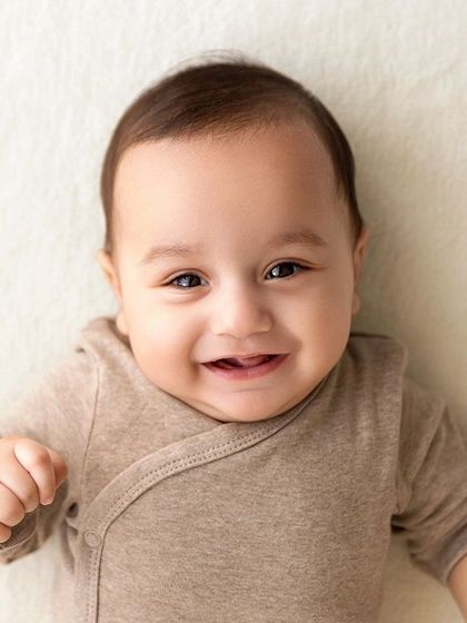 A smiling baby boy lies on his back on a white blanket, a simple and classic baby portrait.