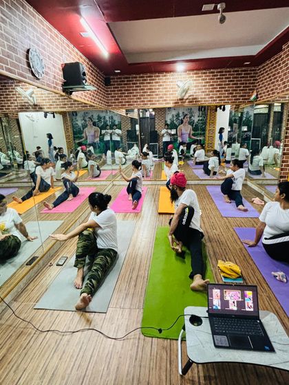 A view of the studio during a seated twist practice on Yoga Day. You can see students joining both in-person and online, connected by the practice.