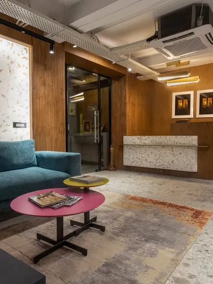 The reception and waiting area at SIRCA HQ features a comfortable teal sofa and colorful coffee tables. The design uses a mix of textures and materials to create a welcoming and stylish first impression.