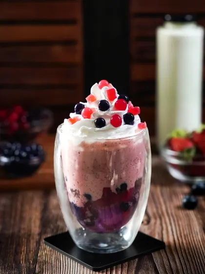 A berry-licious boba tea smoothie topped with whipped cream and colorful popping boba. The dark, rustic setting emphasizes the drink's vibrant colors and indulgent toppings.