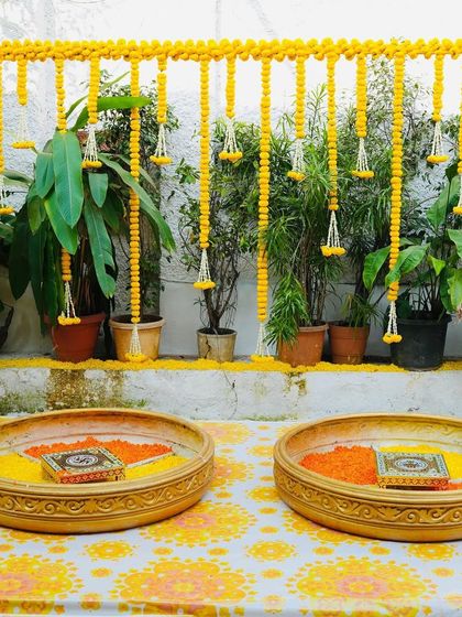 An elegant and simple Haldi setup for an intimate ceremony at home. We used a backdrop of marigold garlands against the home's natural greenery, with brass urlis filled with flower petals for the ritual.
