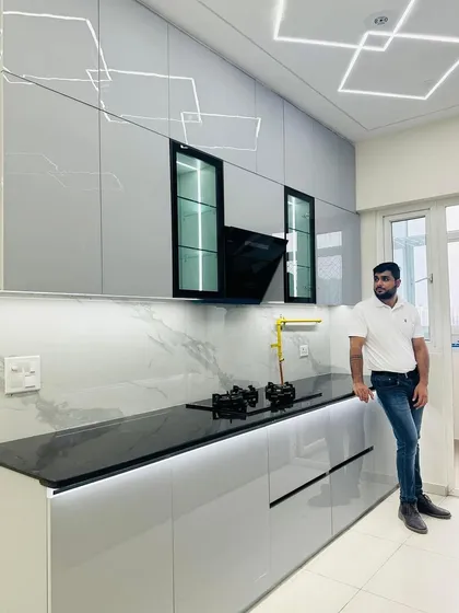 Posing in the newly completed grey modular kitchen. The combination of grey cabinets, black countertop, and marble-patterned backsplash creates a sophisticated look.