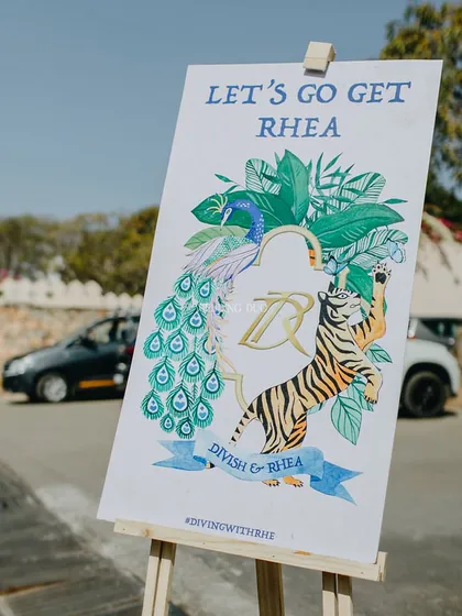 A personalized welcome sign for the groom's arrival, featuring custom illustrations of a peacock and a tiger, along with the couple's wedding hashtag.