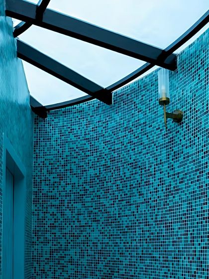 A closer look at the custom metalwork for the skylight and the wall-mounted light fixture, which contrasts beautifully with the shimmering blue mosaic tiles.