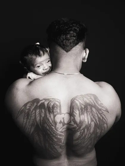 An awake newborn peeking over dad's shoulder, adding a playful and interactive element to this artistic father and child portrait.