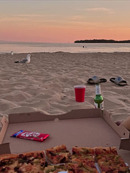An aesthetic shot of a beach picnic with pizza and a sunset view.