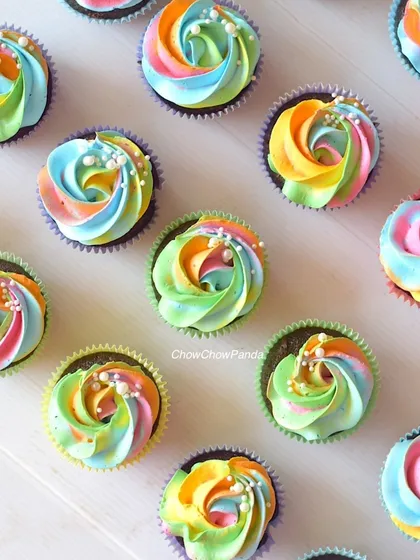 A close-up view of my rainbow swirl cupcakes. The chocolate cupcakes are topped with a multi-coloured buttercream frosting and a light dusting of white sprinkles.