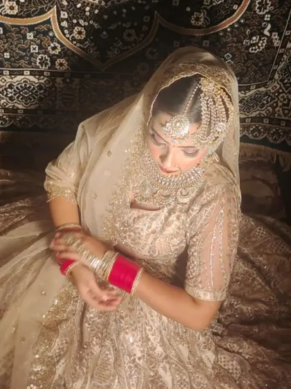 A beautiful shot of a bride in a golden lehenga, showing the intricate work on the skirt and the traditional red chooda bangles.
