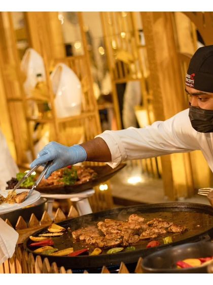 A chef plates a dish for a guest directly from the grill. This direct interaction is a key feature of our service, allowing for a personalized and engaging dining experience.