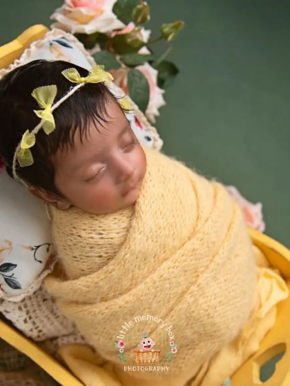 A beautiful shot of a baby girl wrapped in a soft yellow knit. The matching headband and floral pillow add a lovely, coordinated touch.