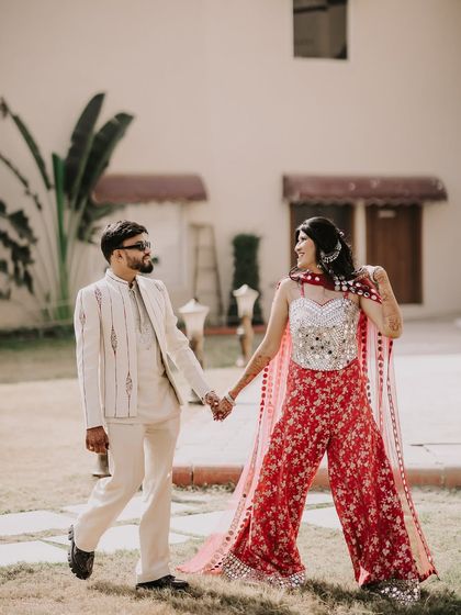 A fun, walking shot from a daytime event. The couple's coordinated red and white outfits pop against the green lawn, and their hand-in-hand stroll shows their easy, happy chemistry.