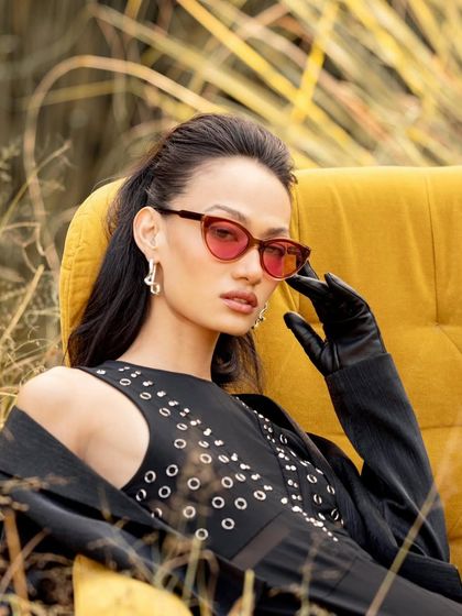 A female model styled with red-tinted sunglasses for the John Jacobs campaign, showcasing a bold and fashionable look.