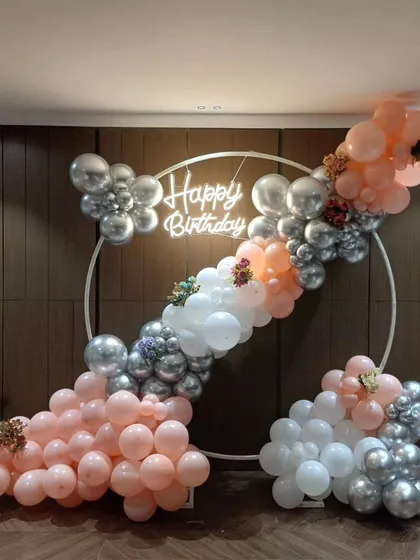 An artistic balloon arrangement on a white ring frame, using peach, white, and silver balloons with floral accents.