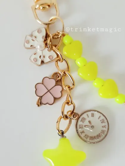 A close-up of the yellow charm keychain, highlighting the cute polka-dot bow and four-leaf clover.