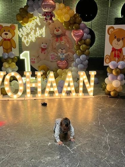 A circular backdrop for a Teddy Bear first birthday, with large marquee letters and a photo of the birthday boy crawling in front.