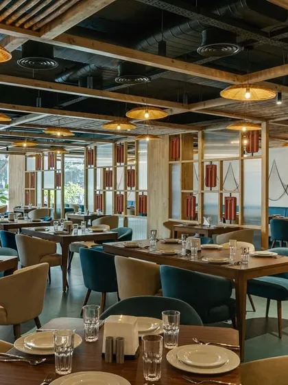 At 'Coast II Coast' restaurant, the design goal was to reflect its coastal cuisine. The continuous pinewood detailing on the ceiling and partitions, combined with a blue and beige color scheme, creates a light, contemporary, and cohesive dining environment.