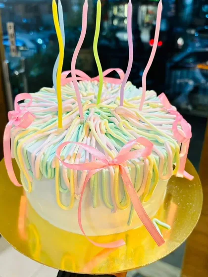 A close-up of one of my custom-designed pastel ribbon cakes. This style is popular for birthdays and celebrations, complete with whimsical, wavy candles.