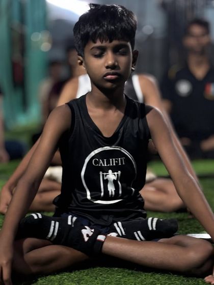 A young athlete in his Califit gear sits in the lotus pose (Padmasana), demonstrating focus and calm during a group meditation.