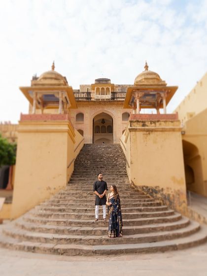 A majestic pre-wedding portrait of a couple standing on the grand staircase of a Rajasthani palace. This shot uses architectural symmetry to create a powerful and timeless image.