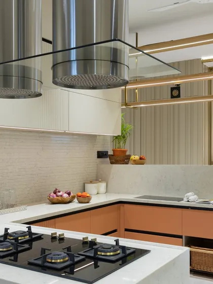 A stunning kitchen with a unique mix of materials. Peach-colored lower cabinets, white upper cabinets, and gold shelving create a warm and luxurious feel, while the dual chimneys add a professional touch.