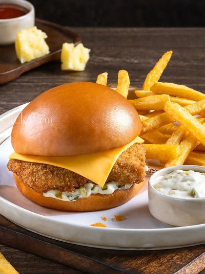 A crispy fish fillet burger with a slice of cheese, served with fries and tartar sauce.