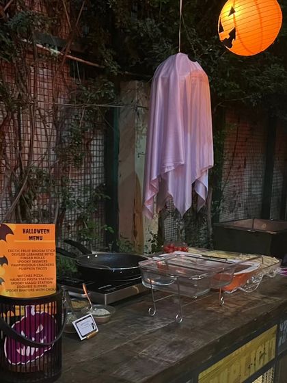 A live food station decorated for Halloween with a hanging ghost and a themed menu. This shows how I transform every element of the catering service to fit your party's theme.