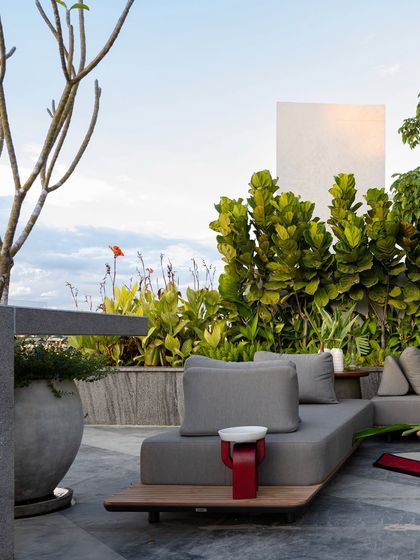 A rooftop garden that balances structured design with spontaneous nature. Sculpted greenery rises behind low, modern seating, while bold red accents and dense foliage offer privacy and a sense of escape.