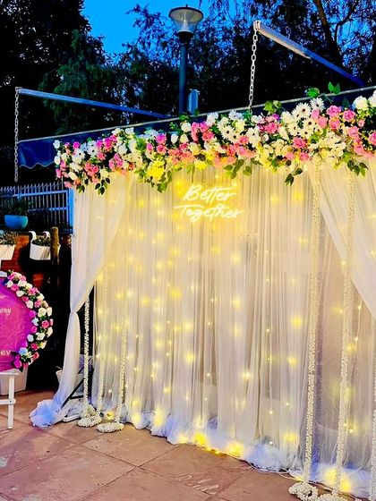 An outdoor evening Roka setup with a beautiful fairy light curtain and a floral top border. The personalized welcome sign adds a thoughtful touch for the guests and the couple.